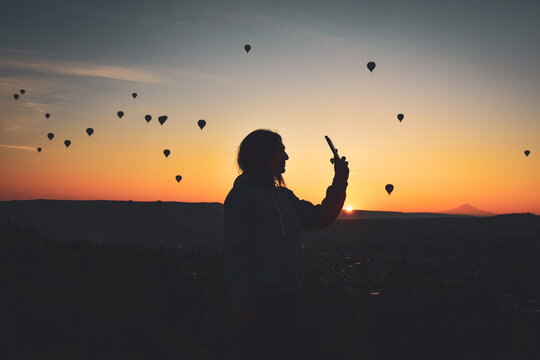 Silhouette of Smart phone in hands of woman taking pictures of a beautiful landscape and balloons in Cappadocia. Sunrise time, dreamy travel concept