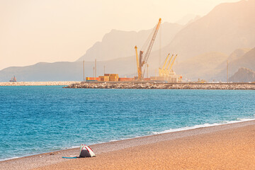 Working construction and industrial cranes at city cargo sea port with ships against mountains background at sunset. Shot taken from Liman beach