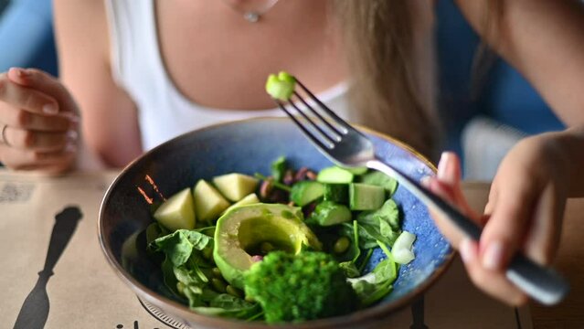 Woman eating healthy green bowl with soia beans, cucumber, leaves, avocado and olive oil