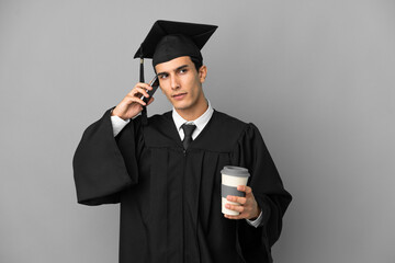 Young Argentinian university graduate isolated on grey background holding coffee to take away and a mobile