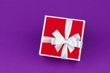 Red gift box with white ribbon on purple background