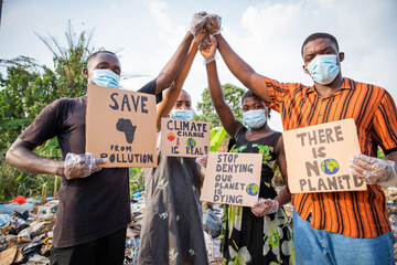 Four young adults protest with signs against pollution outside an illegal open landfill in Africa.