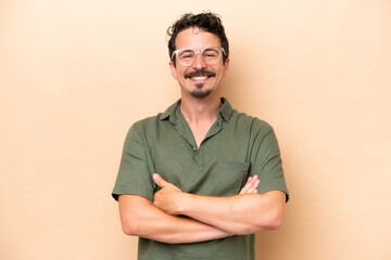 Young caucasian man isolated on beige background keeping the arms crossed in frontal position