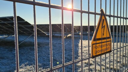 fence of a solar power plant in winter with sign stating in German 