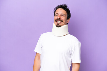 Young caucasian man wearing neck brace isolated on purple background laughing