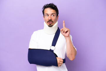 Young caucasian man wearing a sling and neck brace isolated on purple background thinking an idea...
