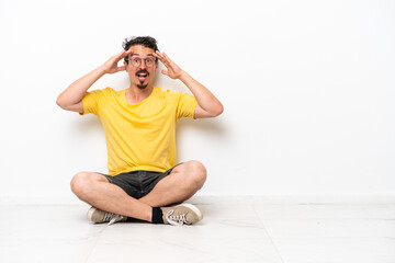 Young caucasian man sitting on the floor isolated on white background with surprise expression