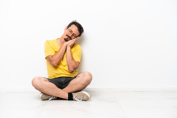 Fototapeta na wymiar Young caucasian man sitting on the floor isolated on white background making sleep gesture in dorable expression