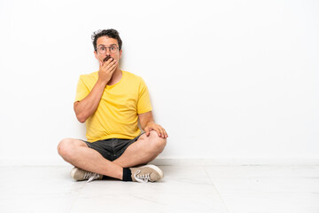 Obraz premium Young caucasian man sitting on the floor isolated on white background surprised and shocked while looking right