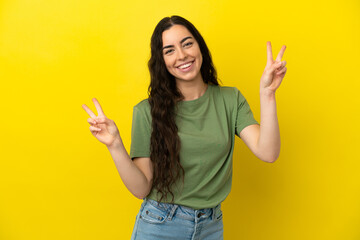 Young caucasian woman isolated on yellow background showing victory sign with both hands