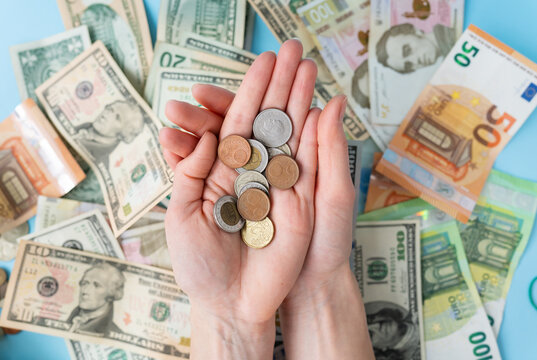 The girl holds coins in her hands against the background of scattered banknotes. International banknotes - dollars, euros, coins. The concept of currency transactions, loans, exchange, gambling.
