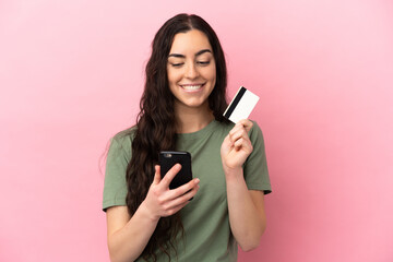 Naklejka premium Young caucasian woman isolated on pink background buying with the mobile with a credit card while thinking