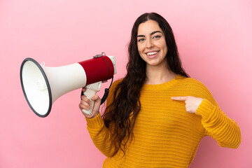 Young caucasian woman isolated on pink background holding a megaphone and with surprise facial expression