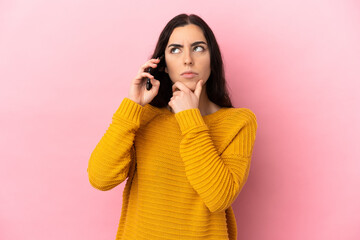 Young caucasian woman using mobile phone isolated on pink background having doubts