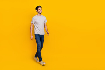 Fototapeta na wymiar Full size photo of optimistic brunet young guy go look promo wear t-shirt jeans sneakers isolated on yellow background