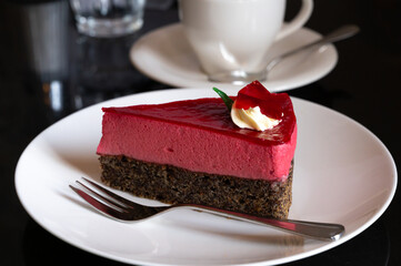 Piece of famous Poppy seed cake with raspberry mousse of Austrian origin served with whipped cream and cup of coffee