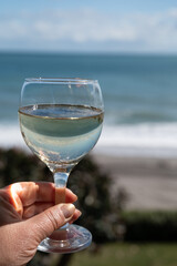 Hand with glass of Spanish dry white wine on beach terrace with view on Mediterranean sea