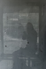 A reflection of a silhouette of a young female hiker sitting at a bus stop (black and white shot)