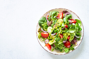 Salad in white plate. Fresh green leaves and vegetables salad. Healthy vegan food, diet food. Top view, copy space.