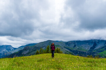 Fototapeta na wymiar A wide angle shot of a young female hiker on a break during a hike on a cloudy summer day in the French Alps (Valberg, Alpes-Maritimes, France)