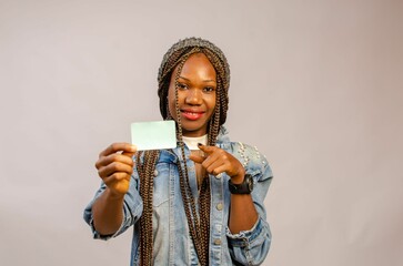 Beautiful Black lady pointing at the identity card in her hand on  a studio background