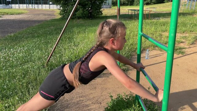 little sports girl trains on the sports ground with a tracksuit, pulls up, pushes up, leads a sports lifestyle
