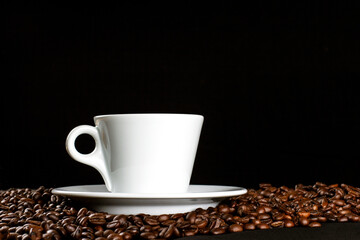 Hot coffee in a white coffee cup and many coffee beans placed around on dark background, with copy space.