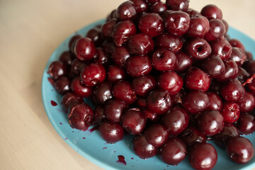 a hill of pitted cherries lie on a plate, on a light background. Delicious, healthy snack, seasonal berries, harvest. The harm and benefits of cherries