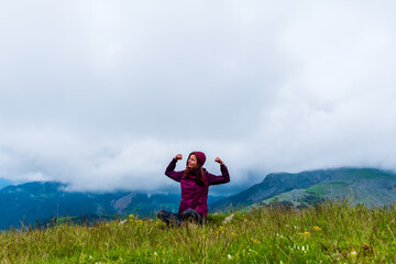 A wide angle shot of a young female hiker on a break during a hike on a cloudy summer day in the French Alps (Valberg, Alpes-Maritimes, France)