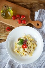 Italian cuisine. Pasta with cheese and white poultry meat. Served in a white plate on a wooden board next to red tomatoes.