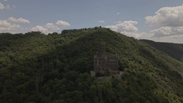 Drone going around the Burg Katz Castle on top of the mountain at evening under shadow of a cloud