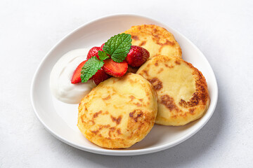 Cottage cheese pancakes with sour cream and berries on a light background. Side view, healthy food.