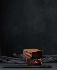 Baked pieces of chocolate brownie pie on black table, delicious dessert