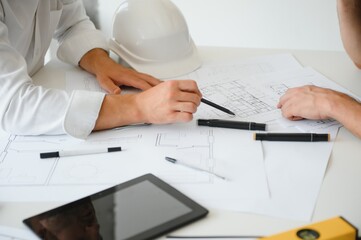 Two engineering working together and using digital tablet looking blueprint and analysis with architectural plan on desk