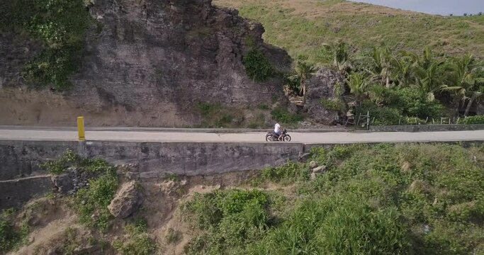 Drone footage of a person riding a bike through a road in the  shore of Batanes, Philippines
