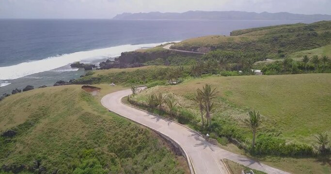 Drone footage of a road passing through the mountainous shore of Batanes, Philippines on a sunny day