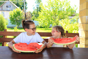 Children eat big watermelon in summer. Satisfied children with a large piece of watermelon on the background of the garden