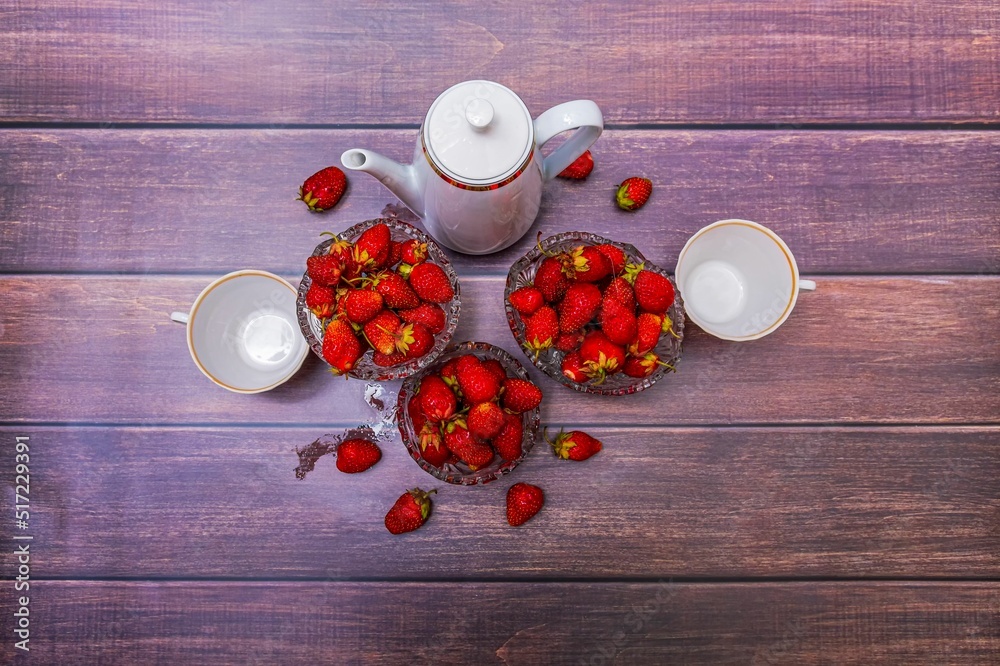 Poster On a wooden table are three vases filled with ripe strawberries, a coffee pot and two empty mugs.