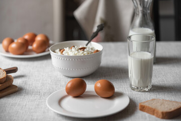 At home, in the kitchen, the table is covered with a linen tablecloth and there are natural and healthy products, milk and cottage cheese, bread and boiled chicken eggs on it