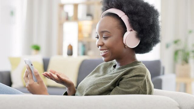 Cheerful african afro woman using phone and headphones and waving while on a video call with friends. Remote student using mobile app and talking to her teacher and learning new language online