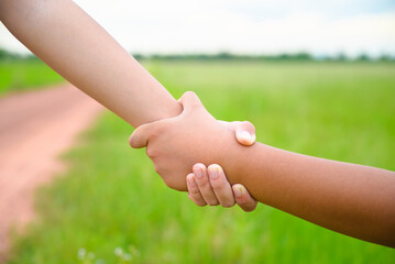 Closeup hand of a young girl trying to pull her friend, grip each other and help him get up from the green field