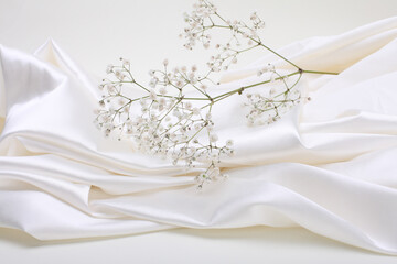 Fototapeta na wymiar White gypsophila flower twig on beige wave fabric silk. Abstract texture horizontal copy space background.