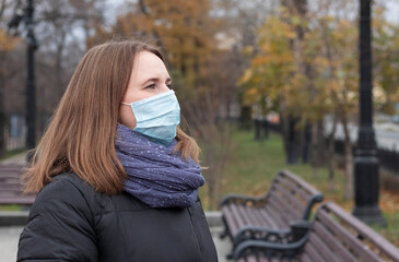 portrait of a young woman in a medical mask in the park in autumn