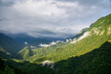 Obraz premium Beautiful landscape in the mounts. Green trees on the hill and clouds over the mountains.