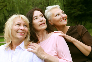 Old people, friendship and emotions concept: Three beautiful elderly ladies are hugging in the park.