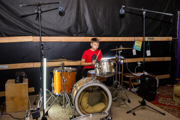 a young drummer plays drums, cymbals with sticks, sitting on a special chair