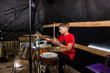 a young drummer plays drums, cymbals with sticks, sitting on a special chair
