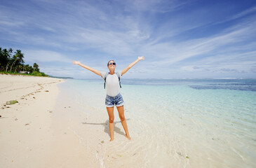 Vacation and freedom. Happy young woman rising hands up standing on tropical beach enjoying beautiful view.