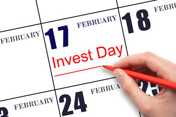 Hand drawing red line and writing the text Invest Day on calendar date February 17. Business and financial concept.