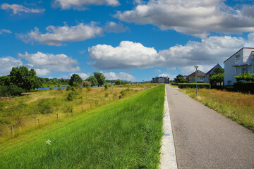 Fototapeta na wymiar Riverside cycle dike path, rural residential area, river Maas, green pasture, blue summer sky - Venlo (Tegelen), Netherlands
